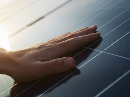 Hand resting on a solar panel sheet on a sunny day.