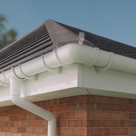 View of a brick-walled house corne with white gutter, downpipe, and black roof.