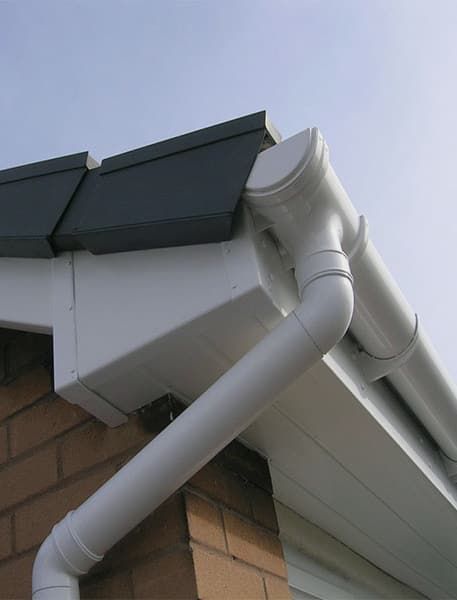 Close shot of a house corner with white downpipes, soffit, and gutters with black roof.