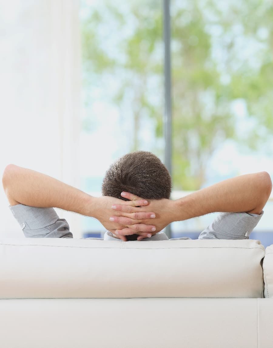 Back shot of man lying back on a couch with his hand behind his head.