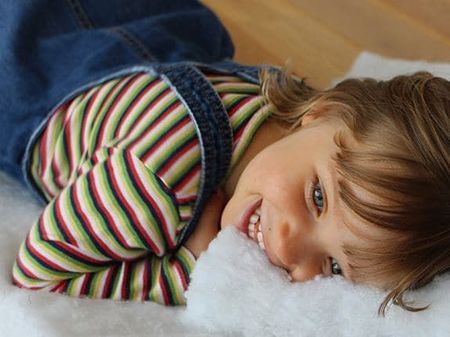 Side view of a girl smiling while lying on cotton insulation sheets.