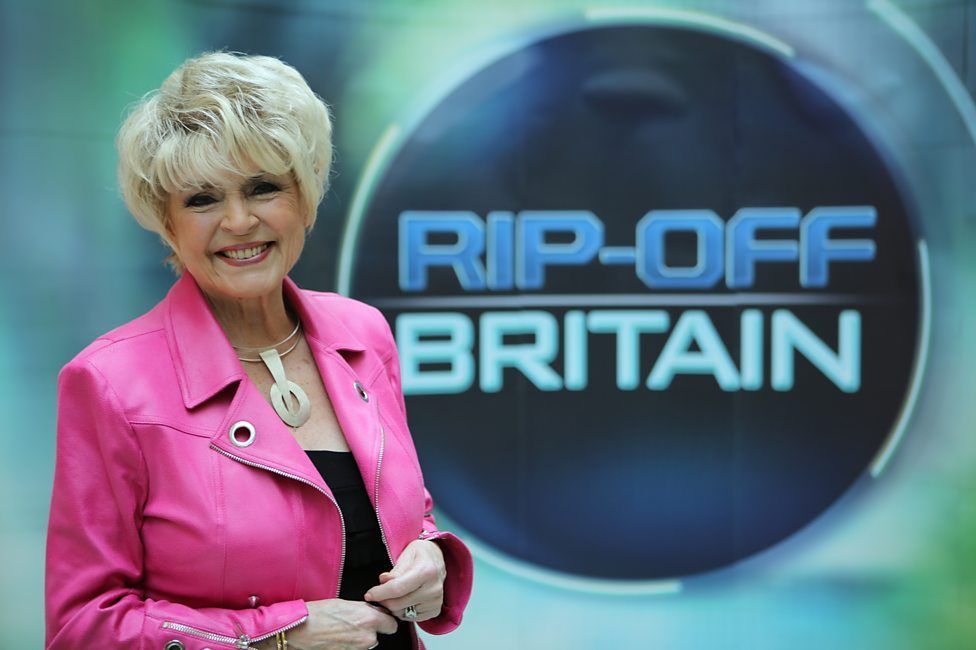 Gloria Hunniford posing in front of RIP-OFF BRITAIN sign.