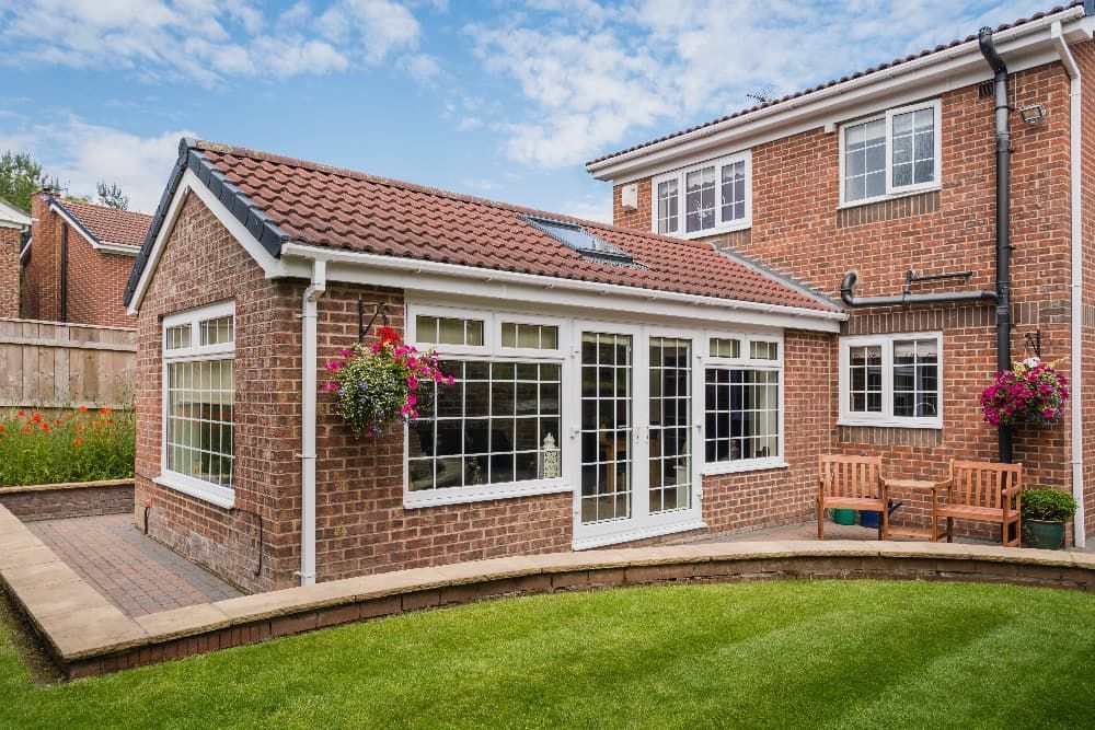 A brick cottage house surrounded by a lawn with a cloudy sky in background.