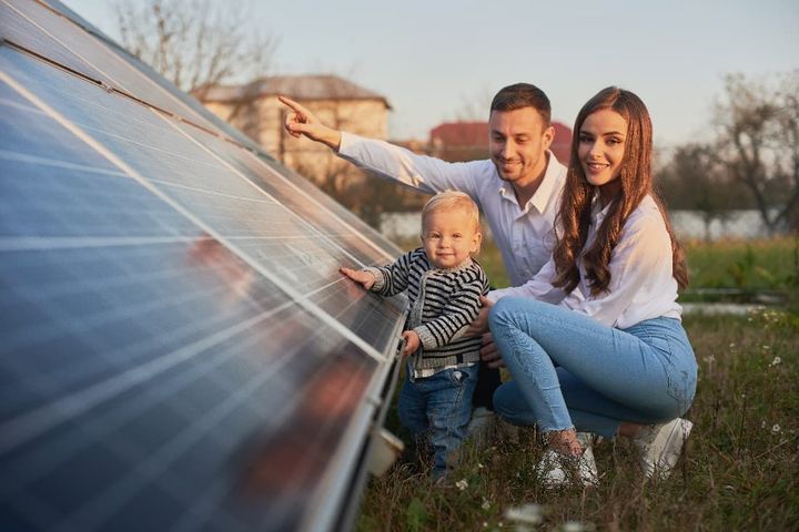 A family of three with a solar panel poses alongside a solar panel sheet.