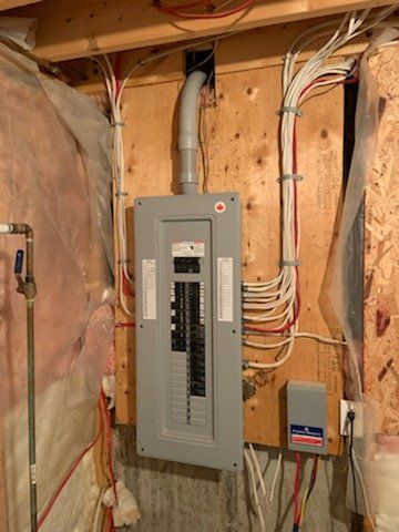 Panneau électrique avec fils et conduits sur un mur en bois dans un sous-sol.