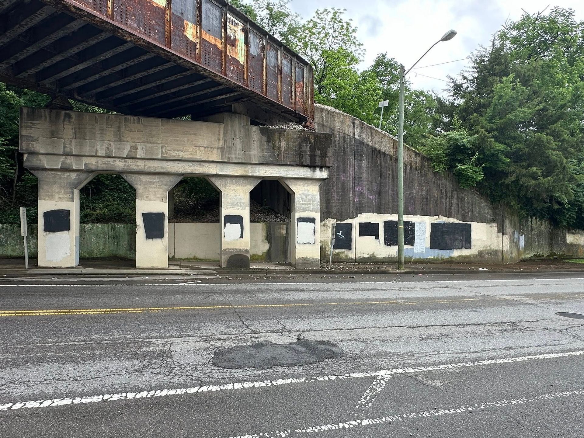 Concrete bridge with a rusty overhead structure over a road. The concrete is stained and has blacked-out openings.