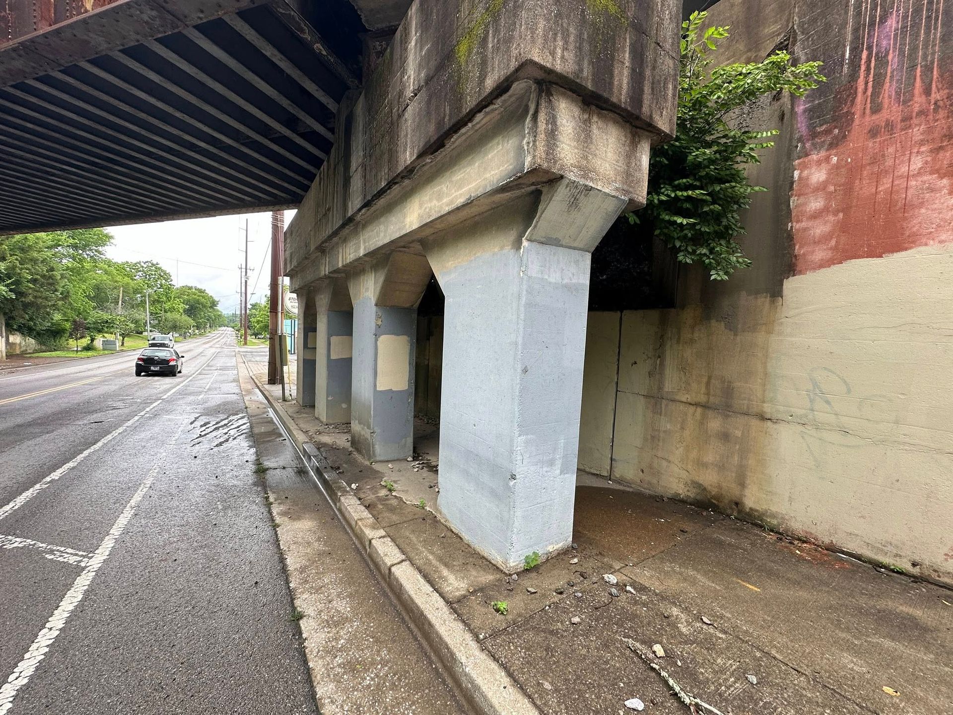 Concrete bridge supports along a road with a car. Gray and beige tones, wet pavement.