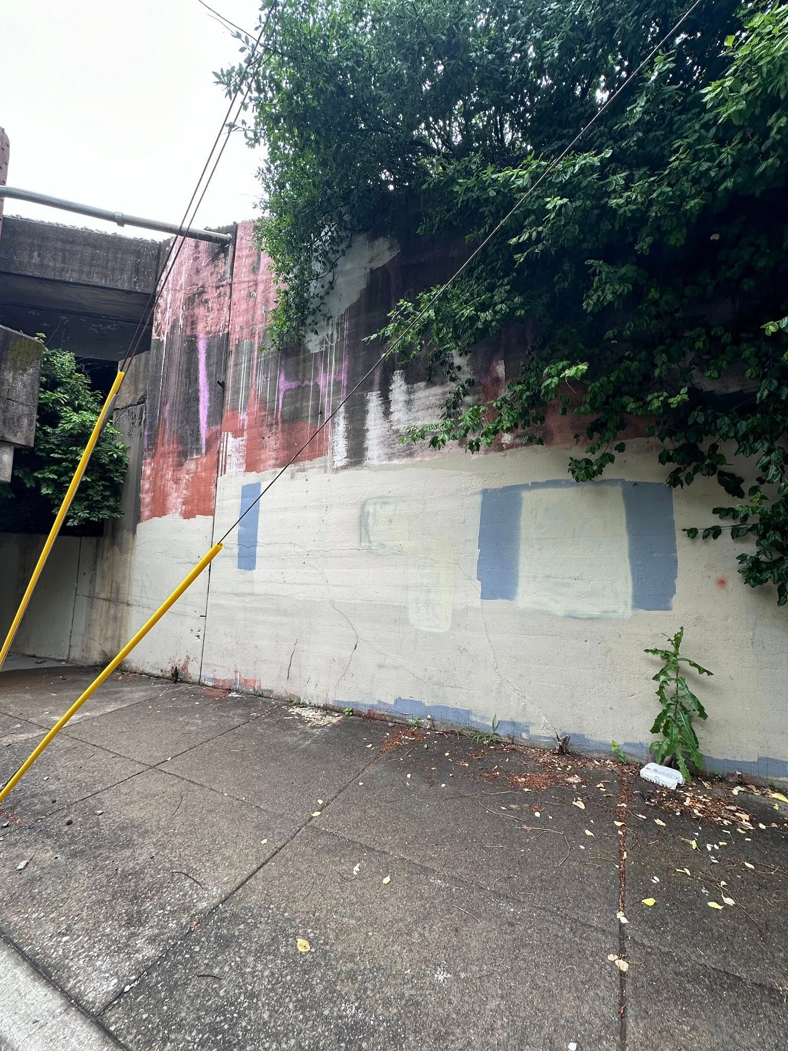 Concrete wall with peeling paint under bridge; gray pavement in foreground.