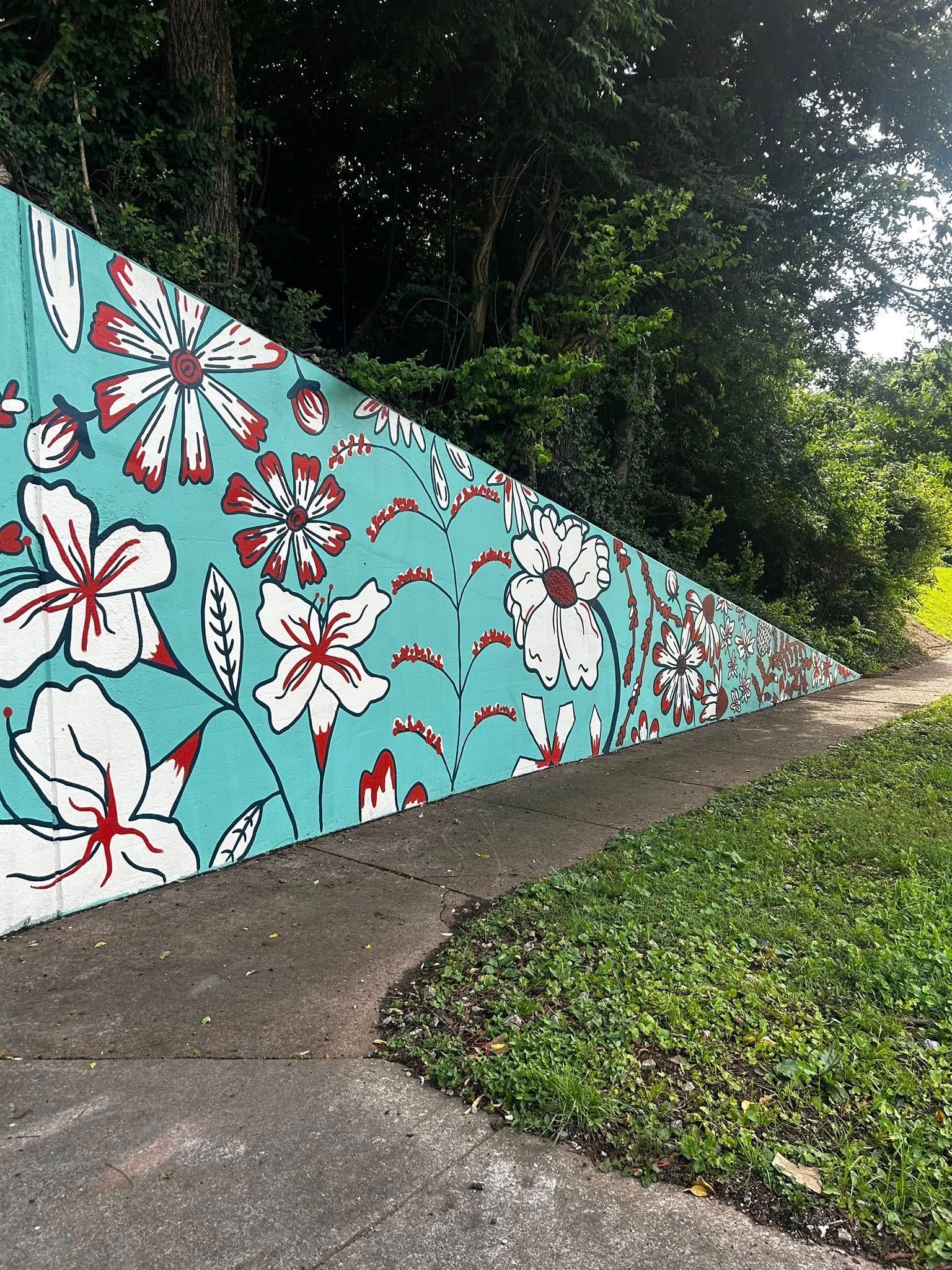 Mural of white and red flowers on a teal background. Concrete path and green grass alongside.