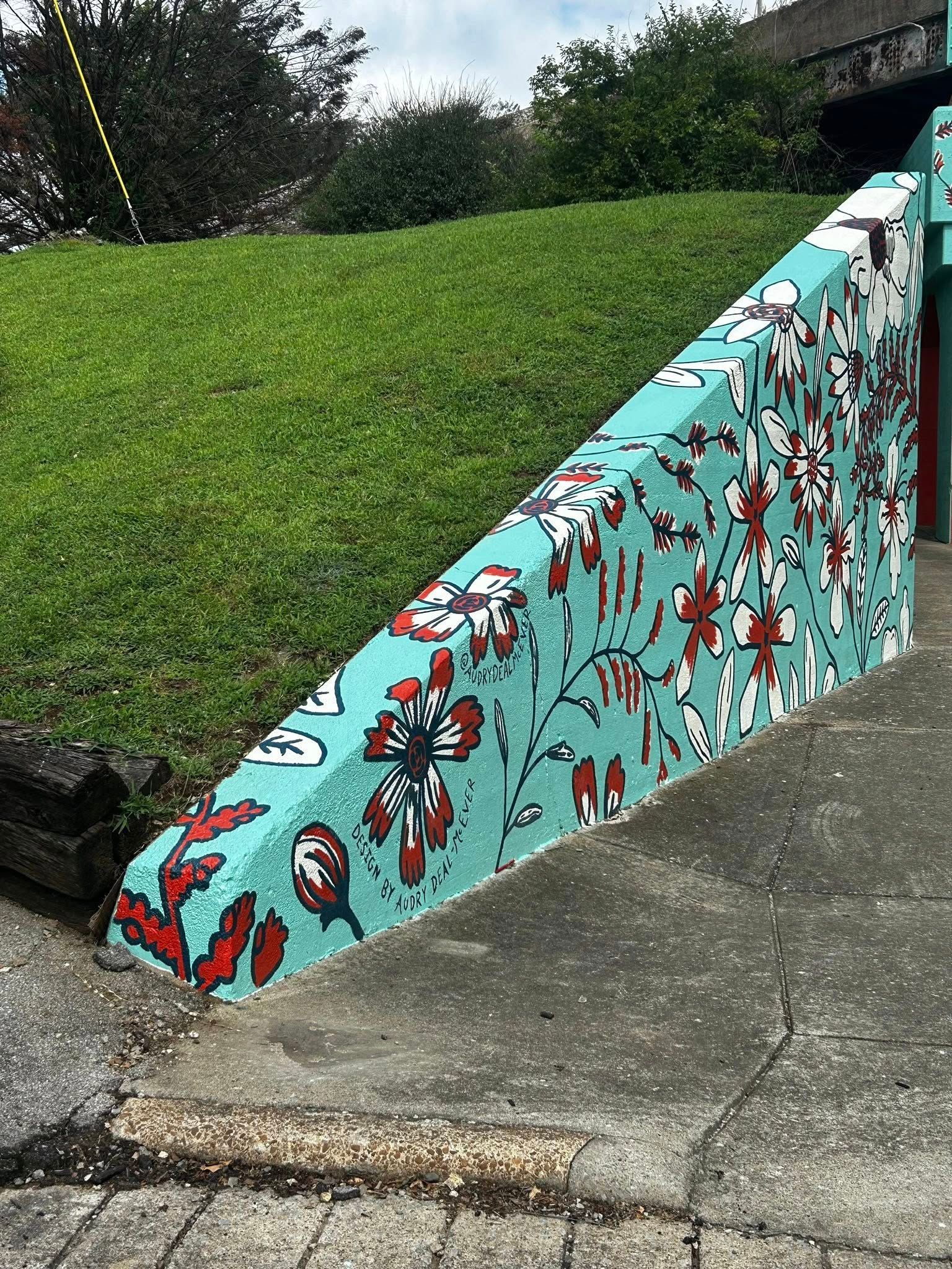 Teal retaining wall with pixelated floral design next to green grassy hill.