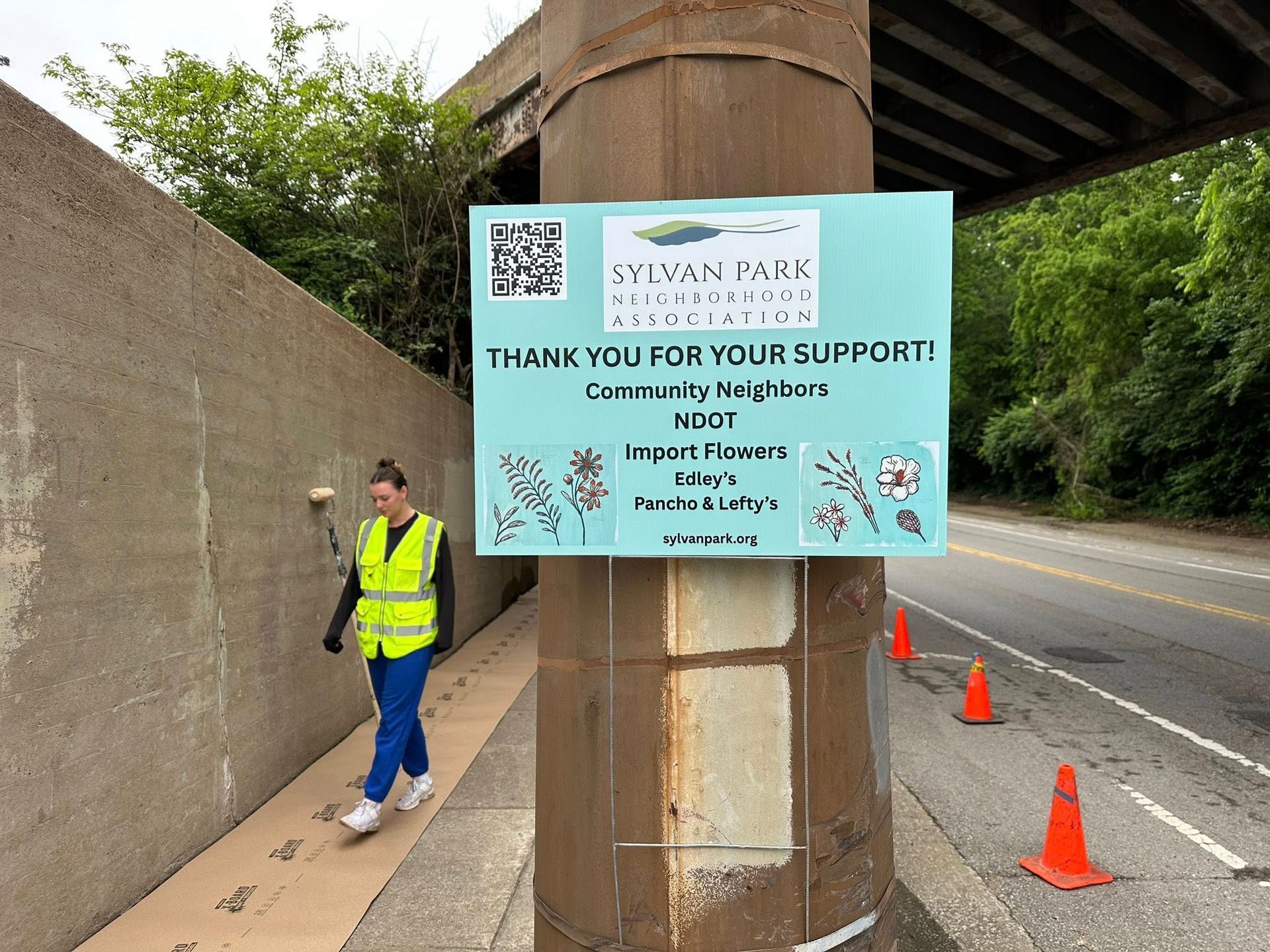 Woman in a safety vest walks past a sign.