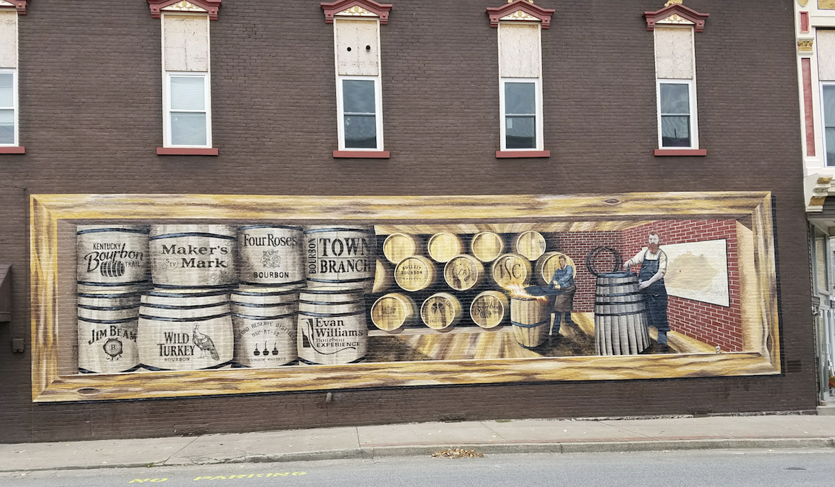 A large mural on the side of a building shows barrels and barrels of whiskey.