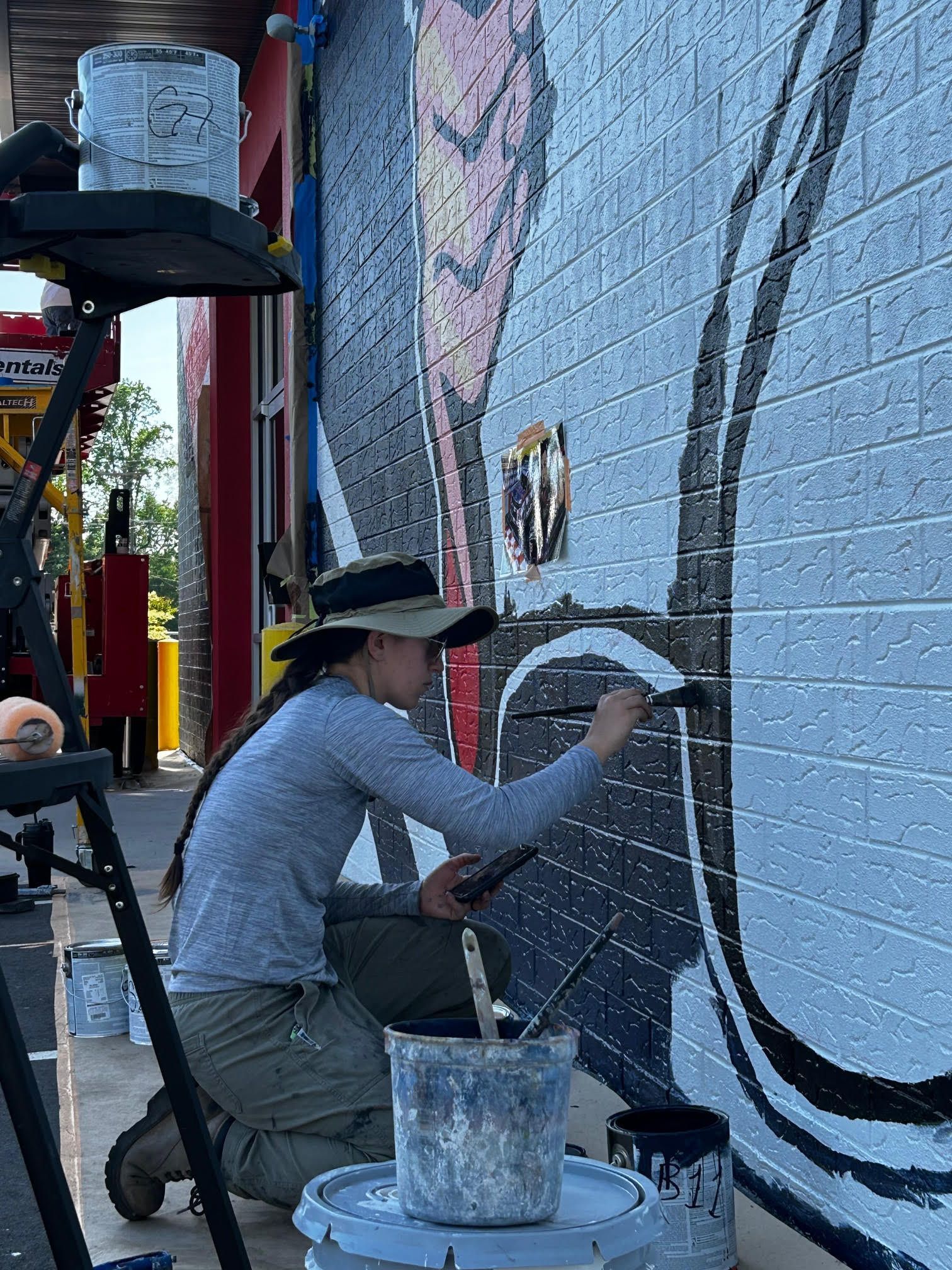 A woman is painting a mural on a brick wall.