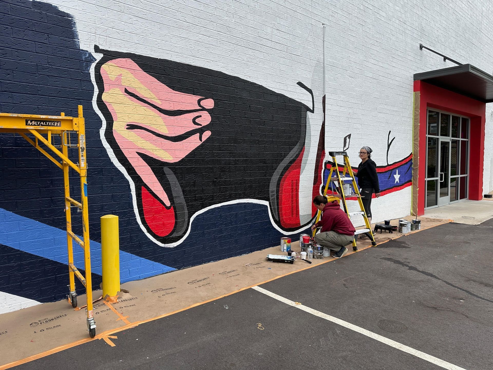 Two men are painting a mural on the side of a building.