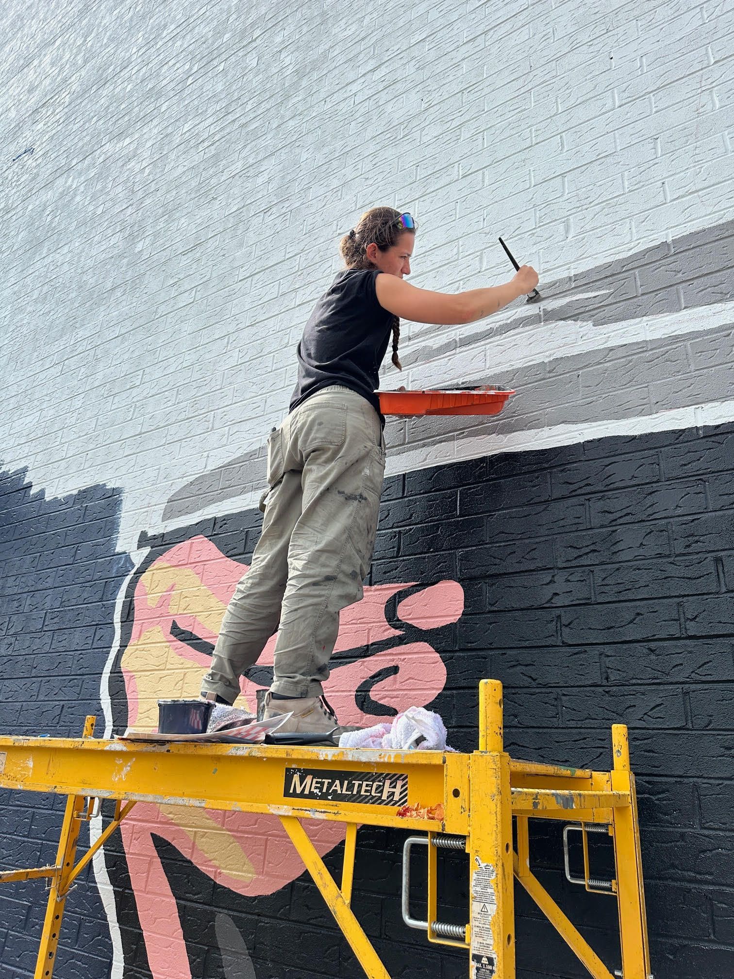 A woman is painting a mural on a scaffolding.