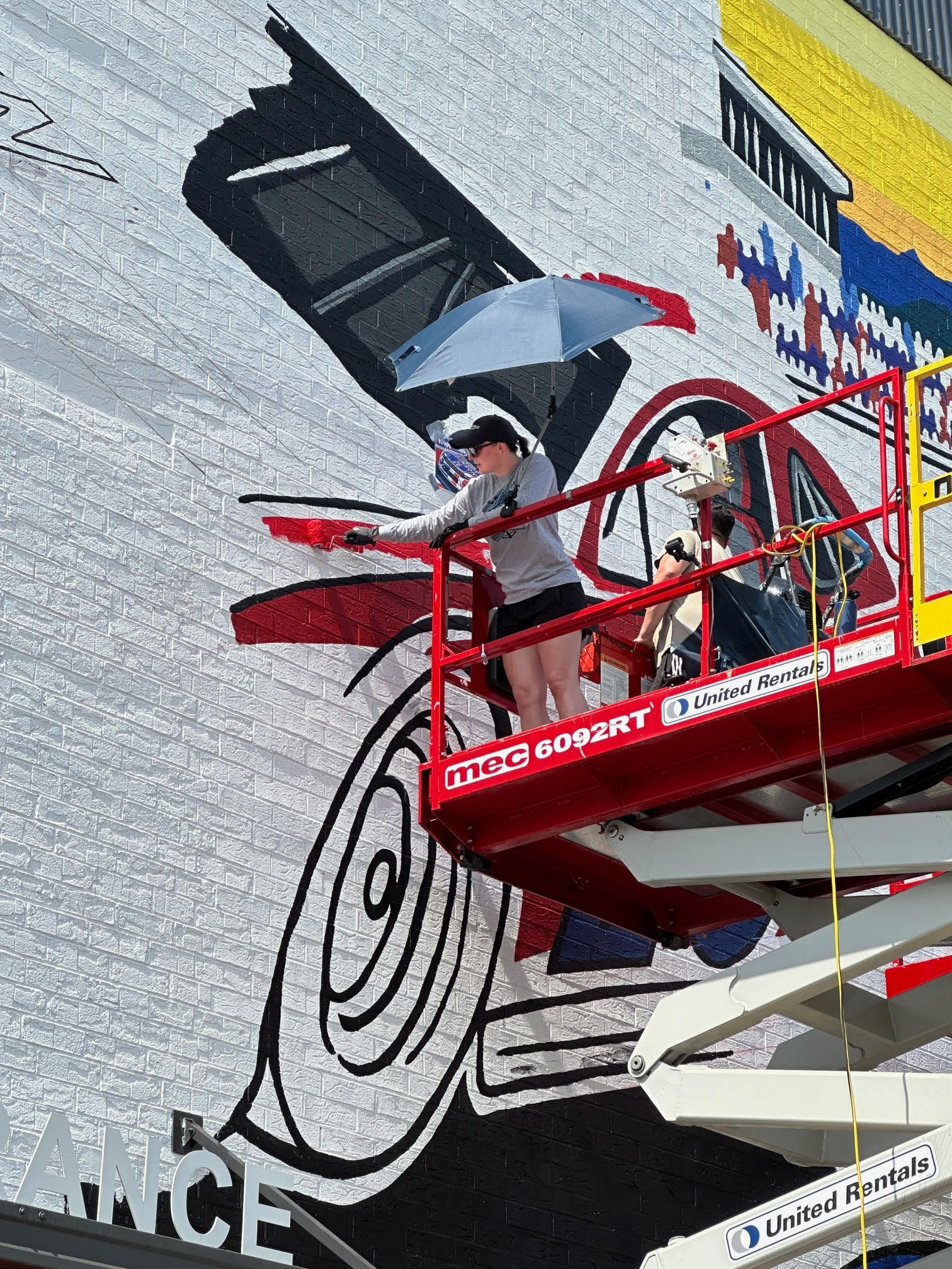 Two people are painting a large mural on a building.