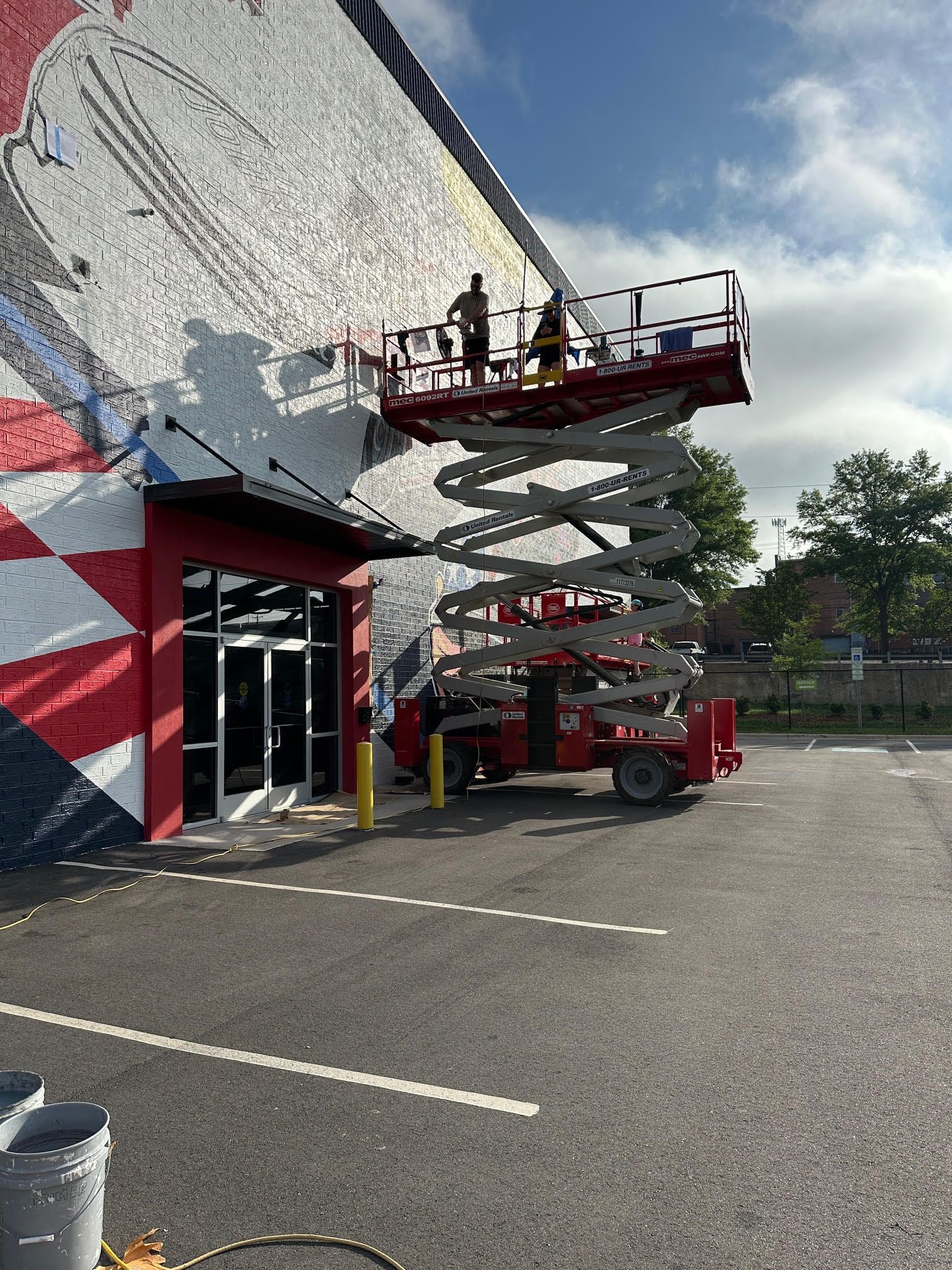 A man is painting the side of a building with a scissor lift.
