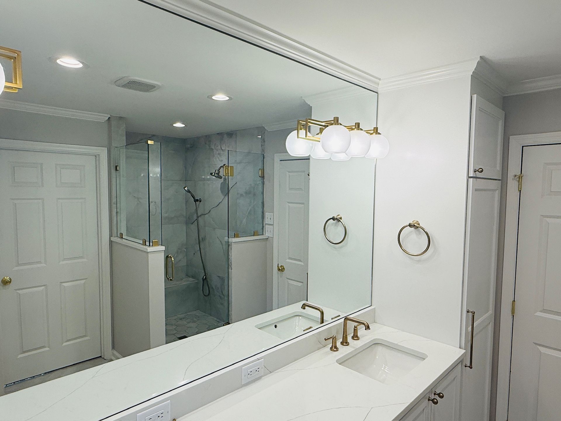 Bathroom with large mirror, white vanity, gold fixtures, and glass shower.