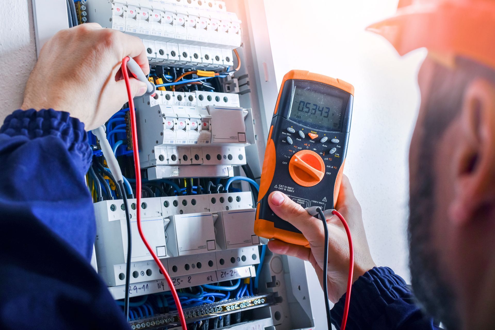 An electrician is working on an electrical box while holding a multimeter.