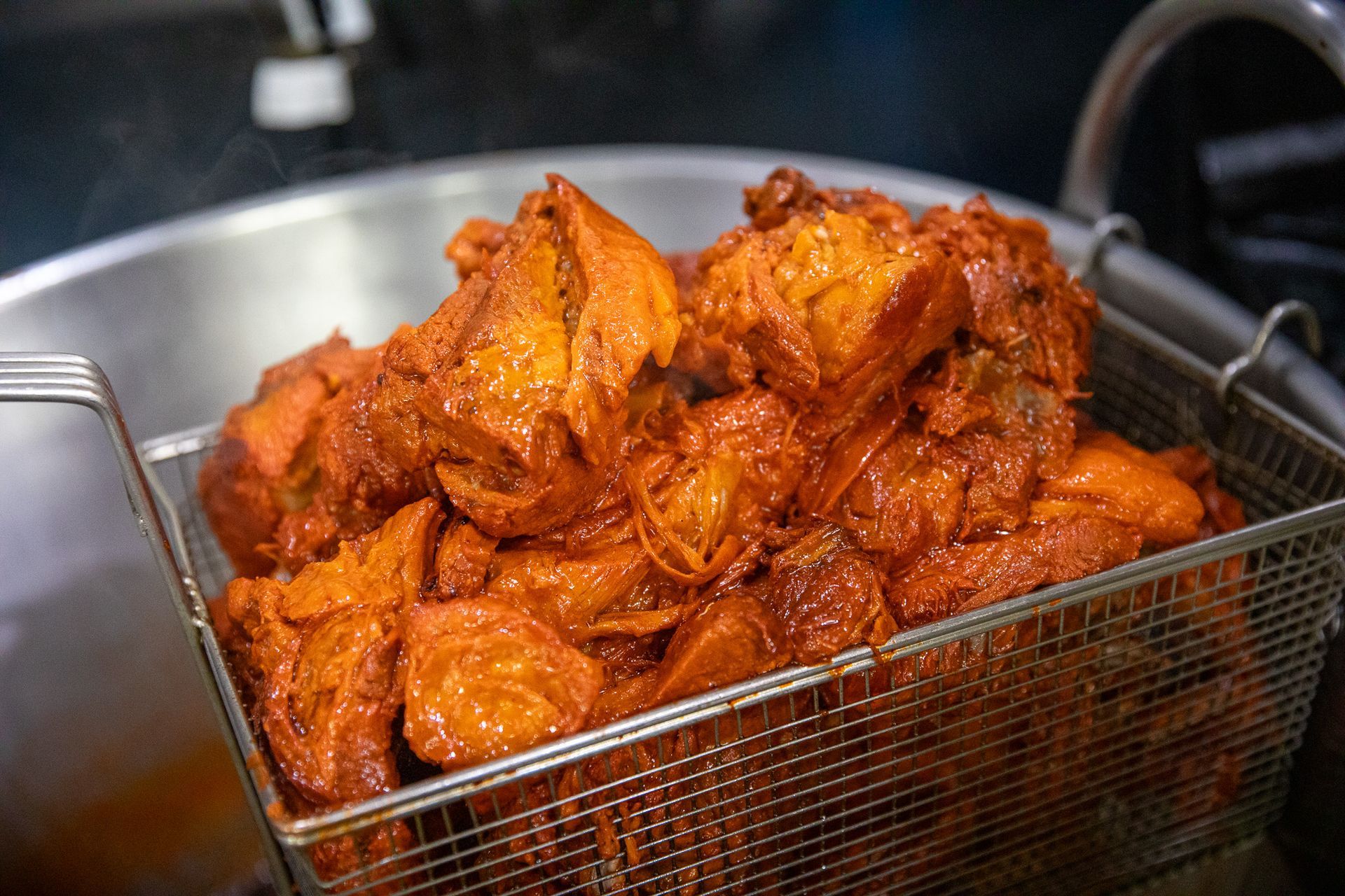 Golden, fried chicken pieces in a wire basket inside a large metal bowl. Steam rises from the food.