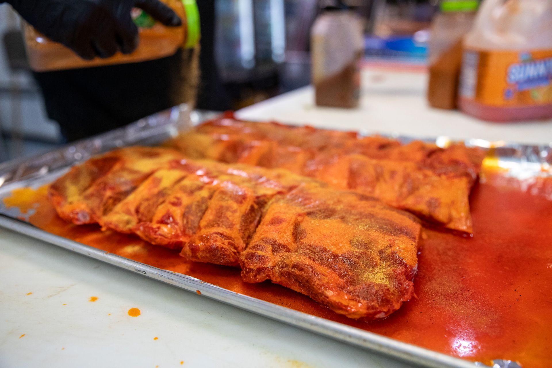 Ribs on a tray being seasoned with orange sauce, prepared in a kitchen setting.