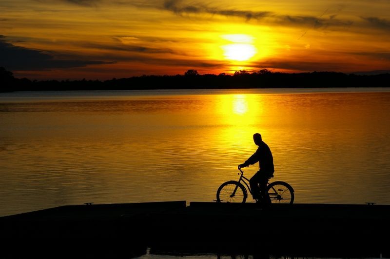 A man is riding a bike on a dock at sunset.