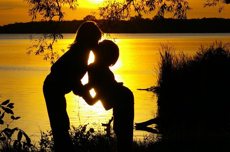 A couple kissing in front of a lake at sunset