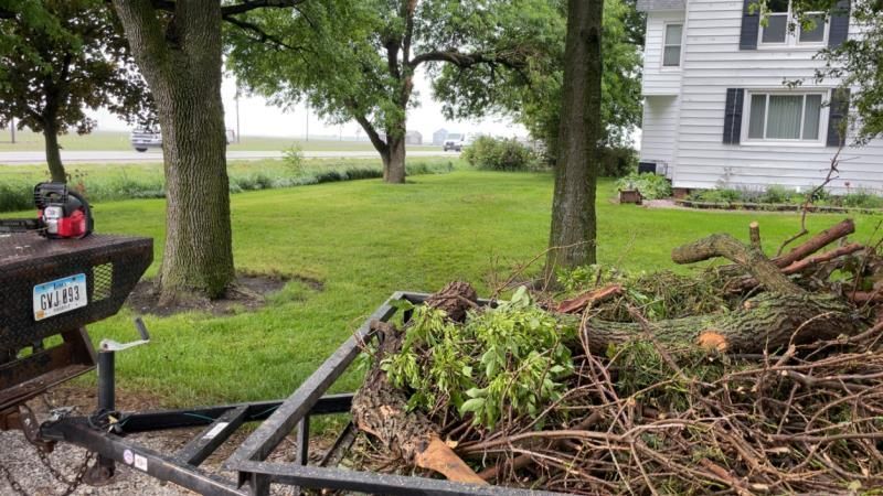 A trailer filled with branches is parked in front of a house.