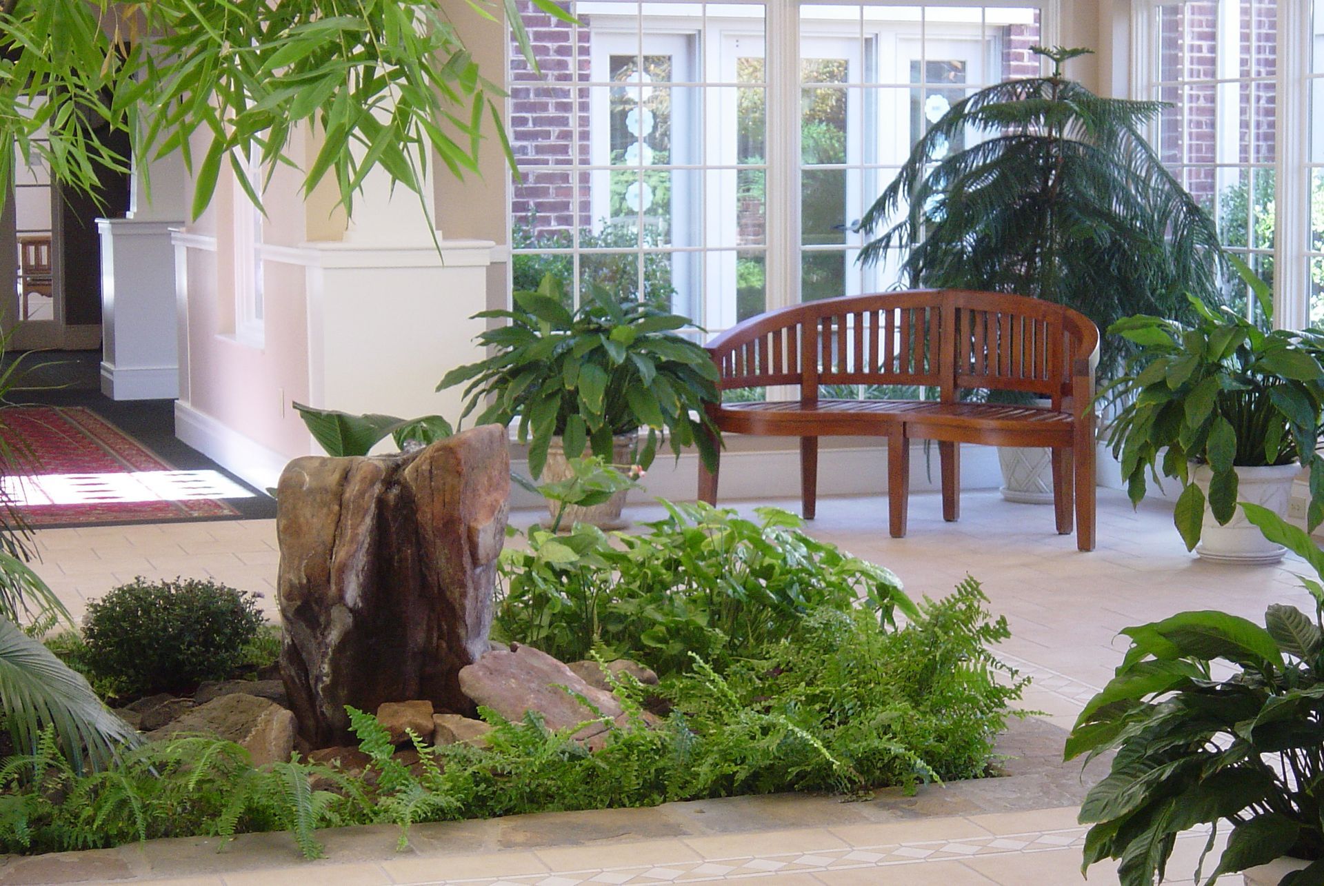 A wooden bench sits in a room surrounded by plants