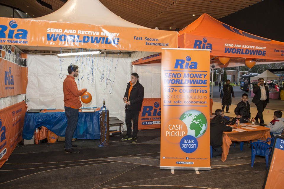 A man is standing in front of a tent that says ria worldwide