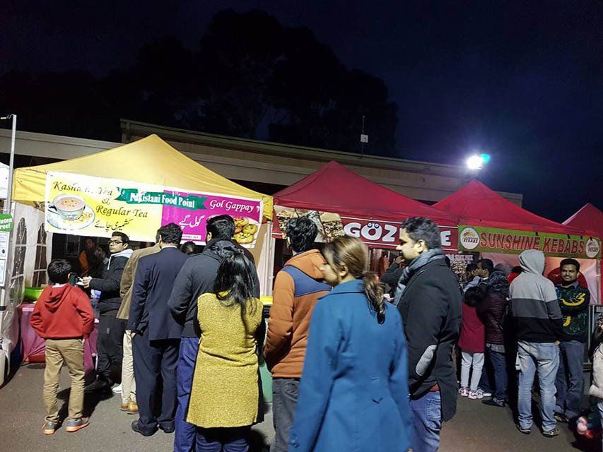 A group of people are standing in front of a food stand at night.