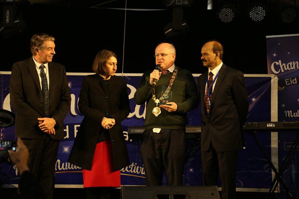A group of people standing on a stage with a man holding a microphone