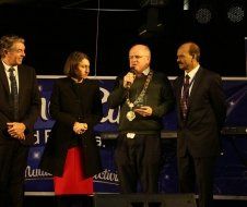 A group of people standing on a stage with a man holding a microphone.