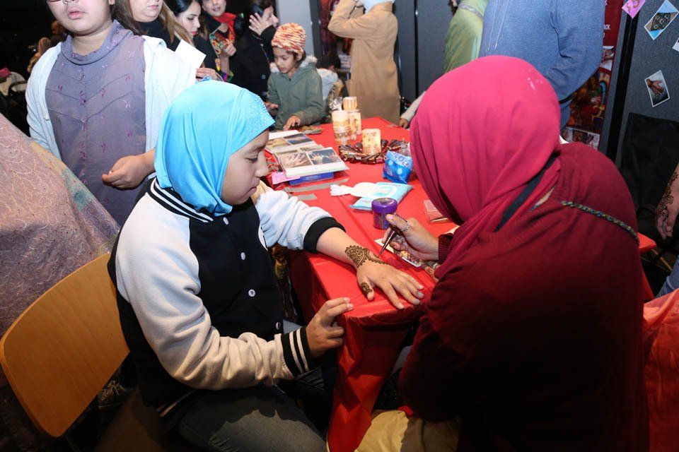 A girl in a blue hijab is getting a tattoo on her arm