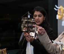 A woman is holding a clock in her hands and pointing at it.