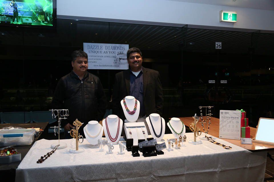 Two men standing in front of a table with necklaces on it
