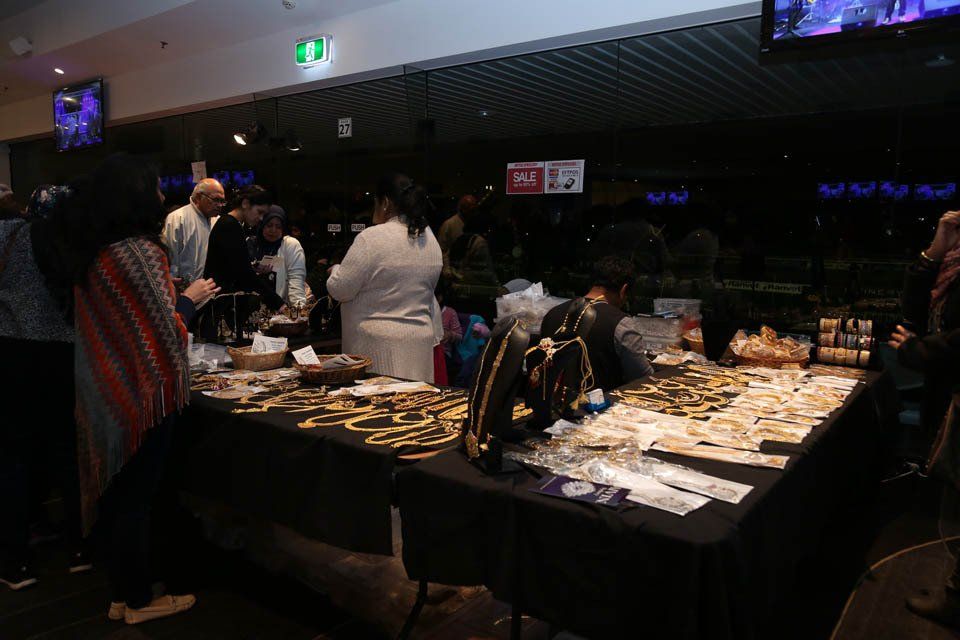 A group of people are standing around a table with lots of items on it.