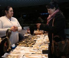 Two women are standing at a table looking at jewelry.