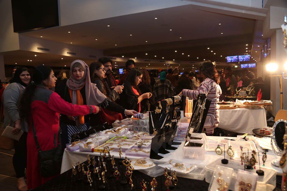 A group of people are standing around a table with jewelry on it.