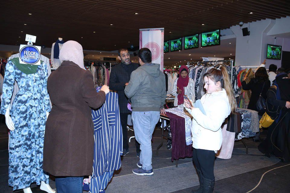 A group of people are standing in a room looking at clothes.