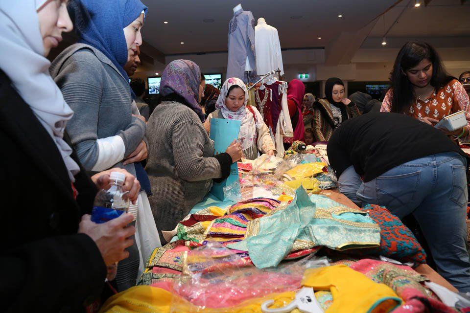 A group of people are standing around a table with clothes on it.
