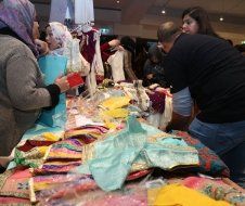 A group of people are standing around a table with clothes on it.