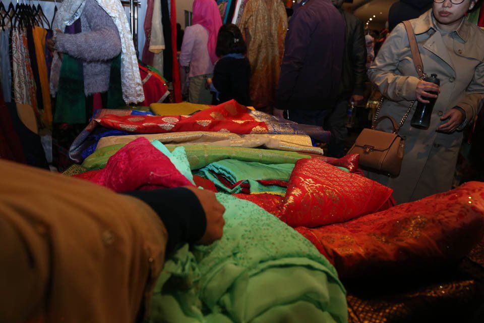 A group of people are standing around a table with clothes on it.