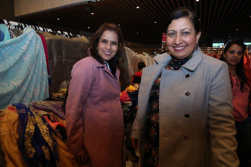 Two women are posing for a picture in front of a display of clothes.