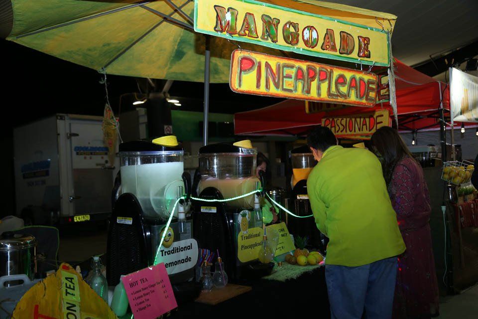 A man and woman are standing in front of a mangoade pineappleade stand