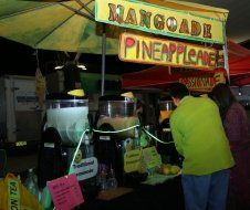 A man is standing in front of a mangoade pineappleade stand.
