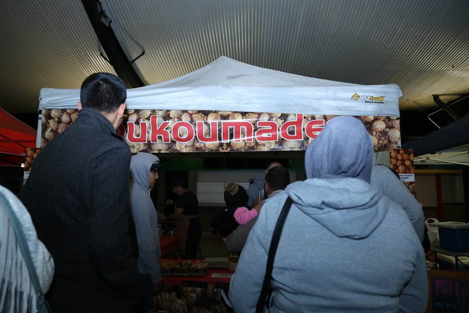 A group of people standing in front of a tent that says ukoumade