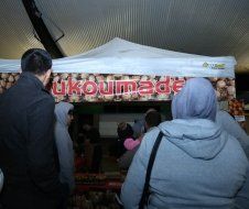 A group of people are standing in front of a tent that says ukoumade.
