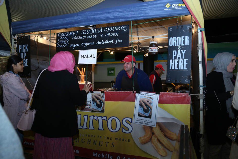 A group of people standing around a food stand that says order pay here