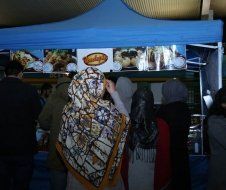 A woman in a scarf is standing in front of a food stand.